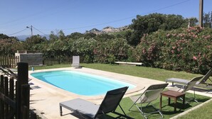 A rectangular swimming pool with a concrete deck, surrounded by a wooden fence. There are lounge chairs and a small table near the pool. - comfortable rental type f2 in the heart of the vineyard with swimming pool  (Patrimonio)