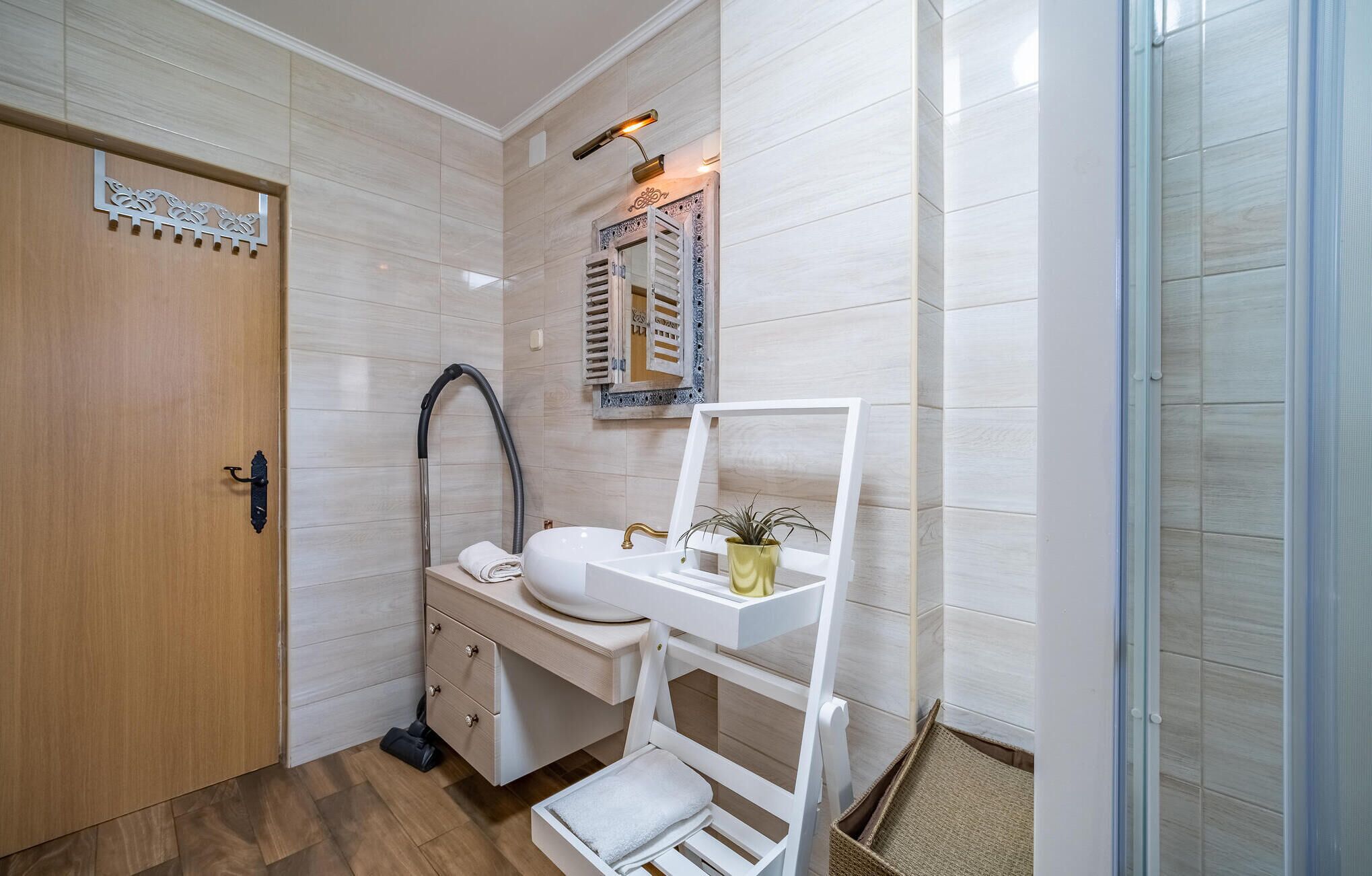 Un baño con puerta de madera, un lavabo blanco con espejo, un perchero y una zona de ducha.