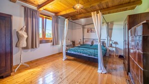 Un dormitorio con techo de madera, una cama con dosel, un maniquí y un ventanal con cortinas.