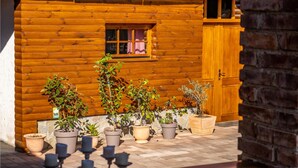 Una cabaña de madera con ventana y puerta. Hay plantas en macetas en el frente.