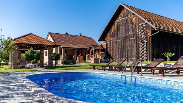 Una piscina con sillones de descanso, un granero de madera y un patio cubierto.
