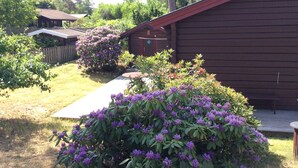 A wooden cabin with a red roof, surrounded by a garden with purple flowers and a wooden deck. - Fantastic family vacation 600m from sandy beach, large garden, near forest, river (Mellbystrand)