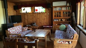 A cozy cabin interior with wooden furniture, a fireplace, a bookshelf, and a window with curtains. - Fantastic family vacation 600m from sandy beach, large garden, near forest, river (Mellbystrand)