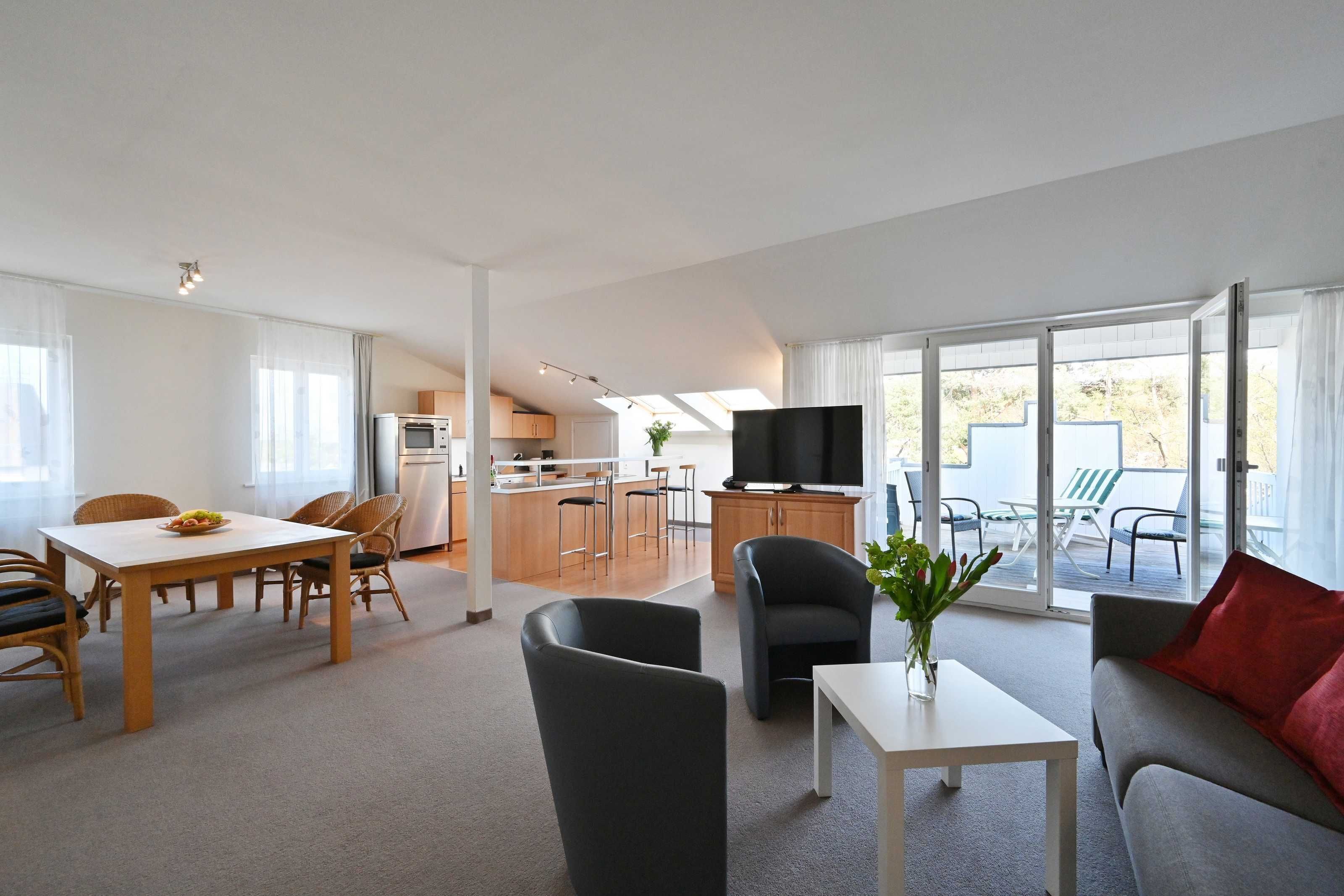 Ein modernes Wohnzimmer mit Essbereich, einer Küche und einem Balkon mit Gartenmöbeln.