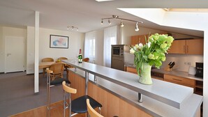 A modern kitchen with a central island, wooden cabinets, and a dining area with chairs. - 6 pers. Apartment 13 Villa Celia Sellin - Villa Celia Sellin (Sellin)