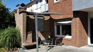 Un patio con una mesa y sillas, rodeado de macetas con plantas y un muro de ladrillo.