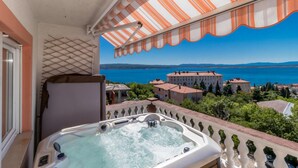 Un balcone con una vasca idromassaggio che si affaccia su una cittadina costiera e il mare.