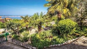 Un rigoglioso giardino con palme e arbusti, un viale in pietra e vista sul mare.