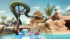 Um parque aquático com um grande tobogã, piscina e um edifício com estrutura em forma de pirâmide.