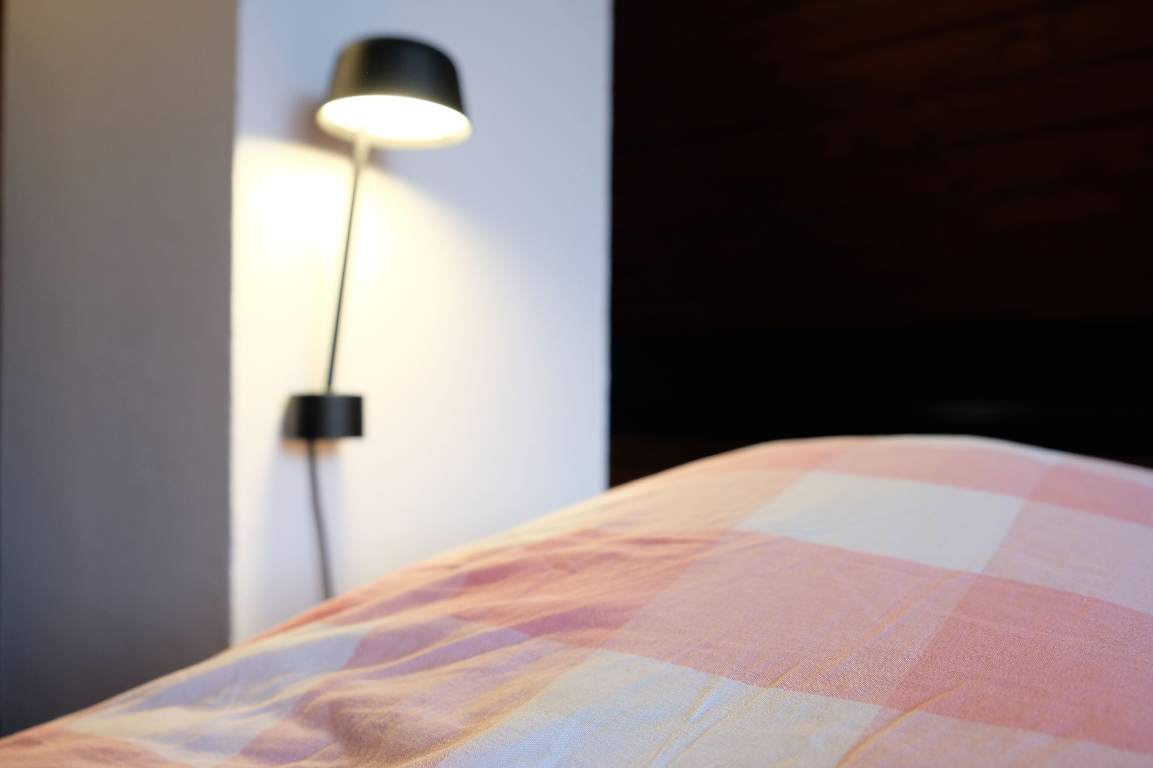 A bed with a checkered blanket and a wall-mounted lamp.