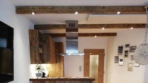 A rustic kitchen with wooden cabinets, a central island, and a dining area with a cowhide rug. - Completely renovated and newly designed apartment (Kirchberg in Tirol)