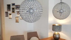 A dining area with a wooden table, two chairs, a chandelier, and a wall with framed pictures. - Completely renovated and newly designed apartment (Kirchberg in Tirol)