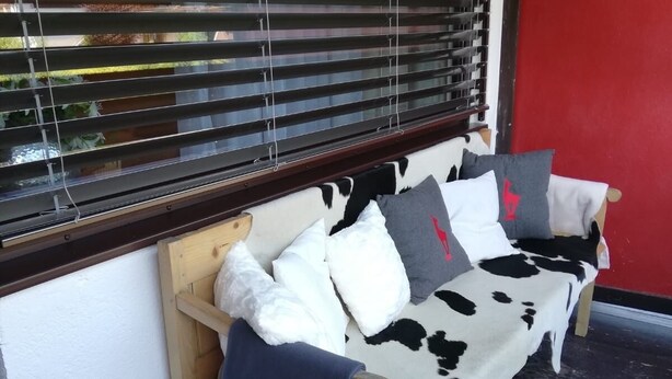 A wooden bench with a cowhide cover and pillows, positioned against a white wall with a red door and a window with blinds. - Completely renovated and newly designed apartment (Kirchberg in Tirol)