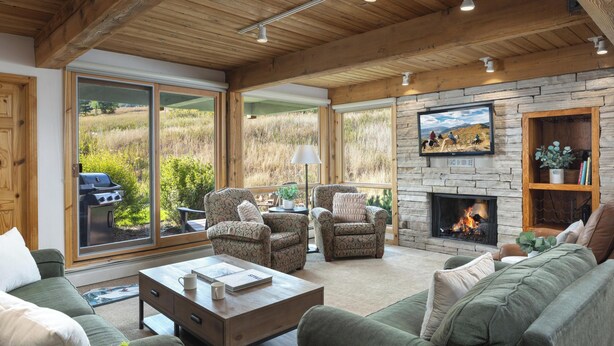 Un salón acogedor con chimenea, asientos cómodos y grandes ventanales que ofrecen vistas al exterior.