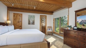 Un dormitorio con una cama grande, techo de madera, cómoda, una silla y ventana con vistas a la montaña.