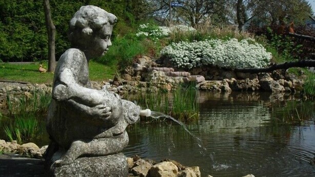 A stone statue of a child sitting by a pond with water flowing from its hand.