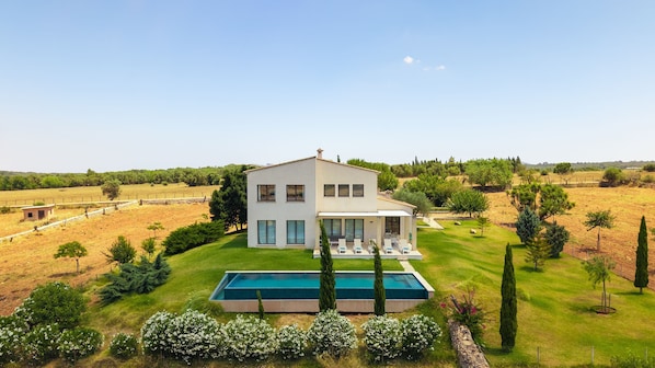 Une maison moderne à deux étages, dotée d’une piscine, entourée d’une pelouse bien entretenue et de divers arbres.