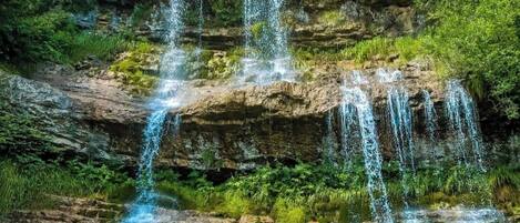 A multi-tiered waterfall cascading over rocky terrain surrounded by lush greenery.