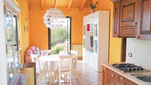 Une cuisine avec un coin repas, des meubles en bois, une cuisinière à gaz et une vue sur l’extérieur par la porte ouverte.