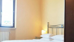 Un letto singolo con struttura in metallo e biancheria da letto bianca in una stanza con soffitto spiovente e una finestra.