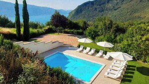 Un espace piscine agrémenté de chaises longues et de parasols, entouré de verdure et de collines.