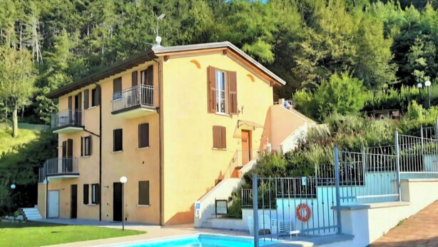 Un edificio su due piani con piscina, immerso nel verde e affacciato su un paesaggio collinare.