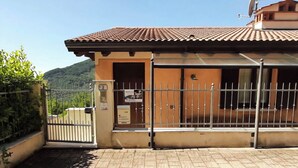 Un edificio con tetto in tegole, ingresso protetto da cancello e montagne sullo sfondo.