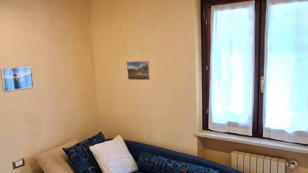 Une pièce avec un canapé bleu, une fenêtre avec des rideaux, un radiateur et un plafond en bois.