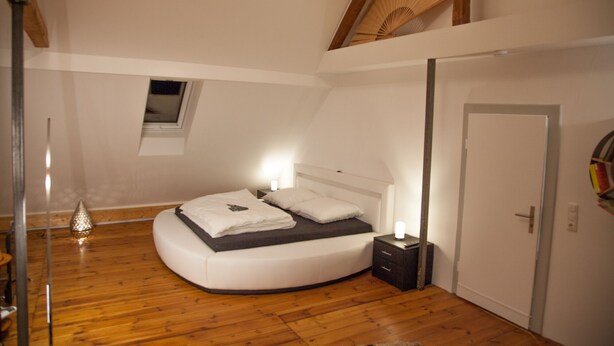 Une chambre à coucher avec un lit à la forme arrondie, une table de chevet avec une lampe, une petite fenêtre et une porte.