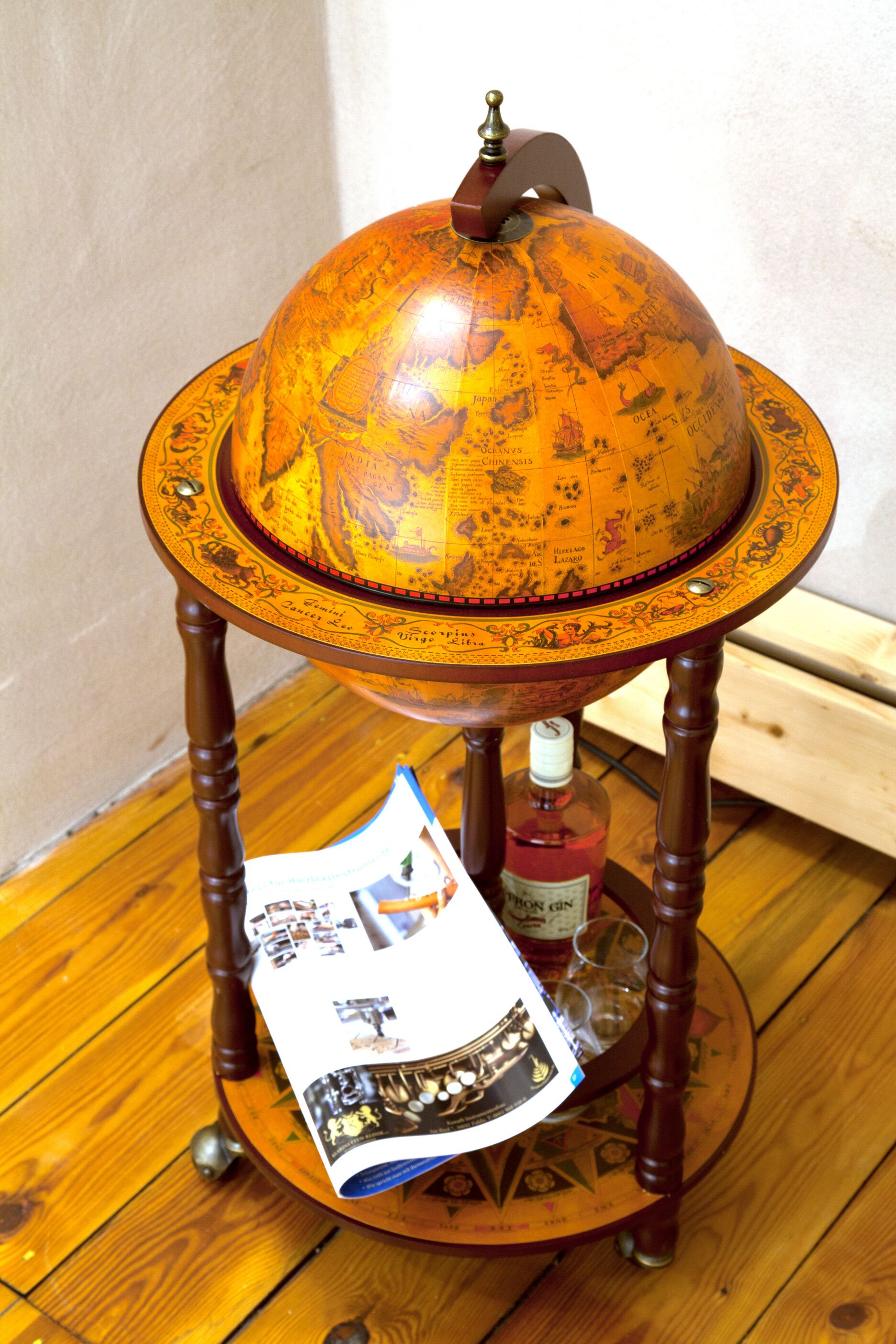 Una mesa con forma de globo de madera, con una botella de ginebra y vasos para chupitos debajo.