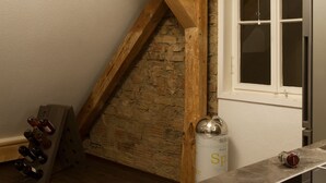 Une cuisine avec un mur en pierre, des poutres en bois, un meuble à vin et un évier en acier inoxydable.
