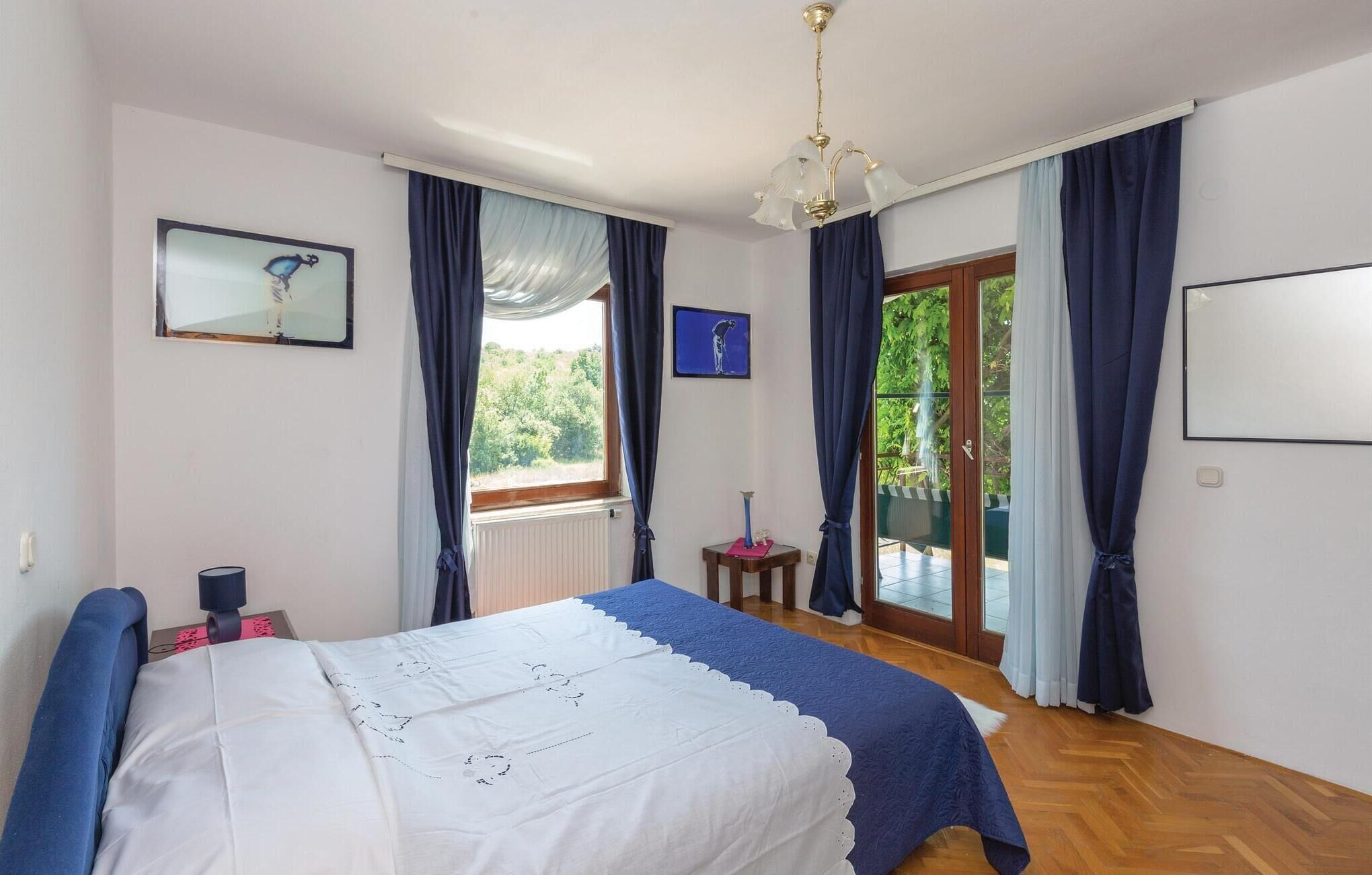 A bedroom with a bed, a window with curtains, a small table, and a picture on the wall.
