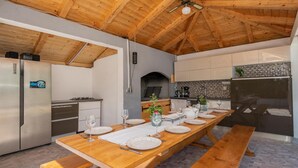 A spacious kitchen with a long wooden table set for dining, a built-in oven, and a refrigerator. - Awesome home in Zmijavci (Zmijavci)