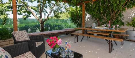 An outdoor patio with wicker furniture, a glass table with drinks, and a pergola with hanging lights.
