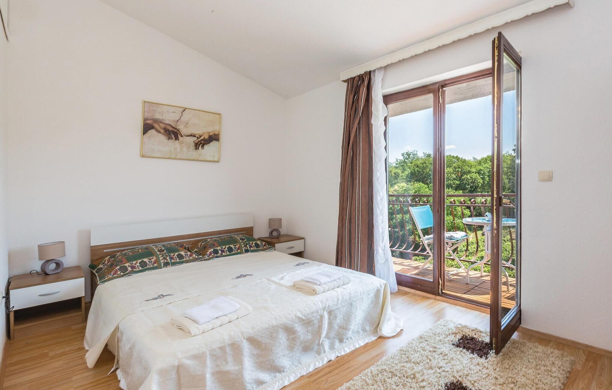 Une chambre à coucher comprenant un lit, des tables de chevet, une commode, un tableau et une vue sur un espace extérieur avec une chaise et une table.