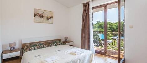 Een slaapkamer met een bed, nachtkastjes, een schilderij en uitzicht op een buitenruimte met een stoel en tafel.