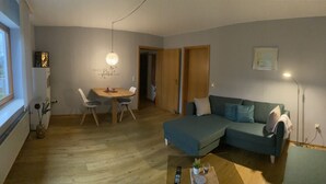 Una sala de estar acogedora con un sofá azul, una mesa de comedor con sillas y suelo de madera.