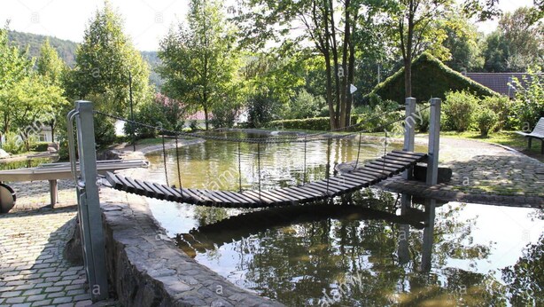 Un puente de madera sobre un estanque con muros de piedra y barandilla de metal.