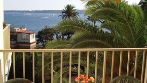 Een balkon met een tafel en stoelen, uitkijkend op een waterpartij en palmbomen.