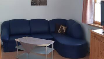 Ein Zimmer mit einem blauen Sofa, einem Glastisch, einem Holzkabinett und einer Wanddekoration mit Pferdemotiv.