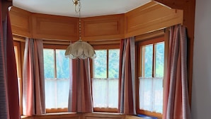 Eine Holzhütte mit Esstisch, Bänken und großen Fenstern mit Vorhängen.