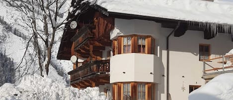 Un chalé de dos pisos con balcón de madera, techo cubierto de nieve y cielo despejado.