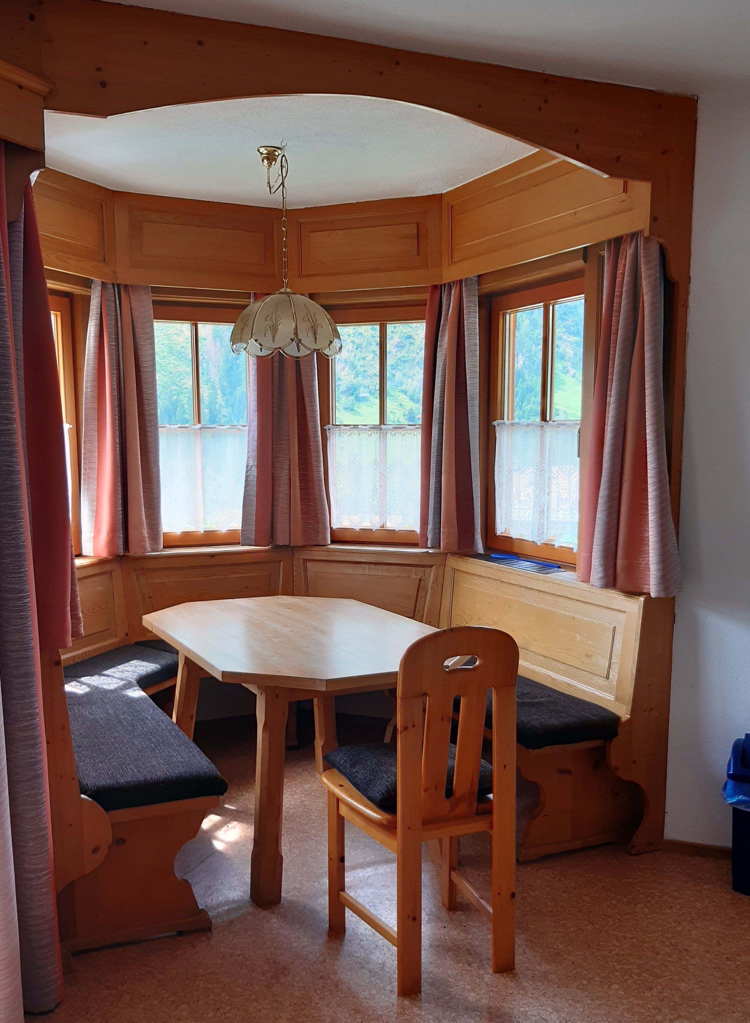 A wooden cabin with a dining table, bench seating, and large windows with curtains.