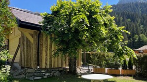 A rustic wooden building with a stone foundation, a white table in the foreground, and a lush tree in the background. - Atypical 2-person chalet "Les Prodains" private parking and free shuttle service (Morzine)