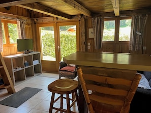 A wooden cabin interior with a dining table, chairs, a television, and a view of greenery outside. - Atypical 2-person chalet "Les Prodains" private parking and free shuttle service (Morzine)