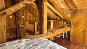 Interior de cabana de madeira com vigas aparentes, uma cama com colcha estampada e uma porta de madeira com design de folha.