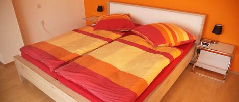 A bed with a wooden frame and a headboard, two bedside tables with lamps, and a wall with a 'You Happy' sign.