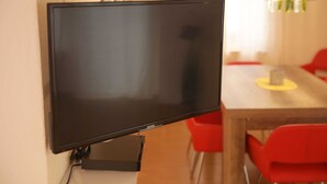 Un téléviseur à écran plat fixé au mur dans une pièce qui contient une table en bois et des chaises rouges.