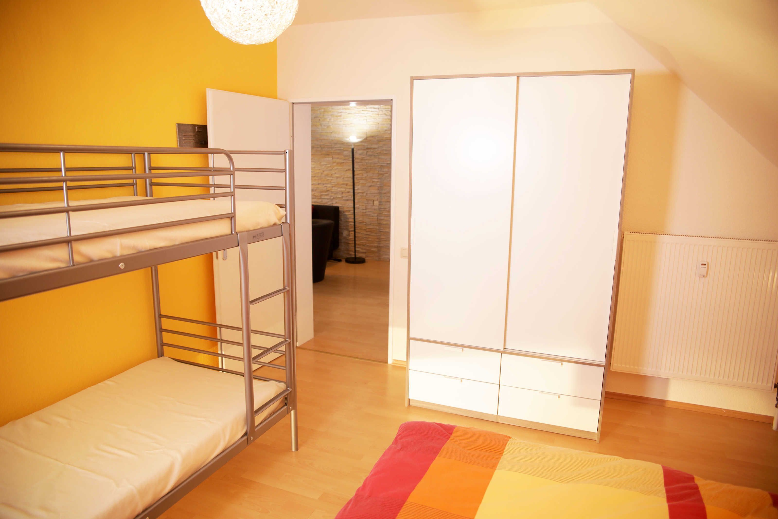 A dormitory room with bunk beds, a wardrobe, and a radiator.
