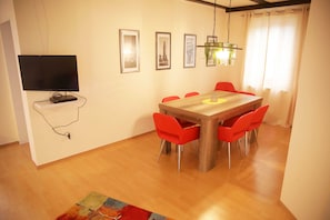 A dining area with a wooden table, red chairs, a flat-screen TV mounted on the wall, and framed pictures on the wall. - ACS 8 - Art City-Studio Kassel 8 (Niestetal)